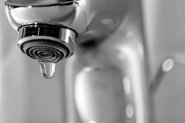 Black and white photo of water droplet coming out of faucet